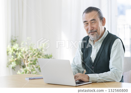 A man in his 70s working on a laptop, looking at the camera, portrait 132560800