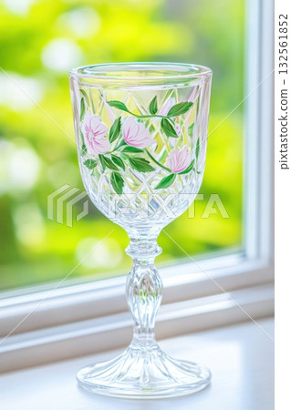 Elegant vintage glass goblet with pastel pink and green floral details illuminated by soft glowing light in a serene setting 132561852