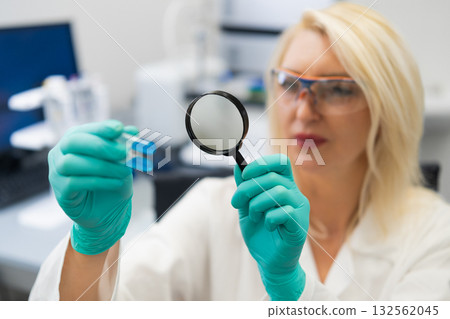 Chemist in laboratory examining chemical solutions in test tubes with magnifying glass. Chemist in laboratory examining chemical solutions in test tubes with magnifying glass. 132562045