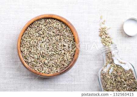 Fennel seeds, in a wooden bowl, on linen. Mistakenly called seeds, fennel fruits are used as food spice, used in cooking, with anise-like taste, and one of the primary ingredients of absinthe. Photo 132563415