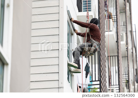 Exterior repair worker rappel down using ropes to repair leaking cement walls residential buildings. Exterior repair worker rappel down using ropes to repair leaking cement walls residential buildings. 132564300