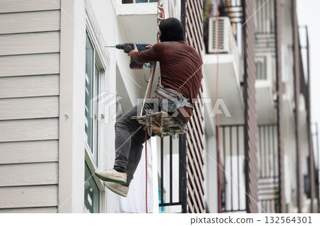 Exterior repair worker rappel down using ropes to repair leaking cement walls residential buildings. Exterior repair worker rappel down using ropes to repair leaking cement walls residential buildings. 132564301