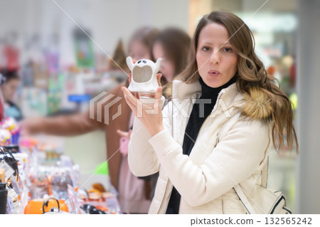 In a lively shopping center, a woman joyfully holds a ghost souvenir while browsing through an array of Halloween gifts, capturing the festive spirit just before the holiday. In a lively shopping center, a woman joyfully holds a ghost souvenir while browsing through an array of Halloween gifts, capturing the festive spirit just before the holiday. 132565242