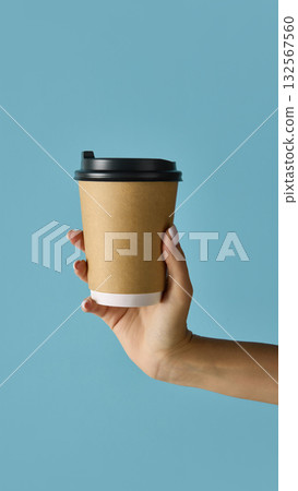 Hand holding brown kraft paper takeaway coffee cup with black lid on blue background Hand holding brown kraft paper takeaway coffee cup with black lid on blue background 132567560