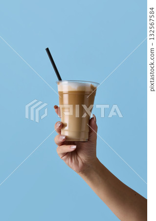 Hand holding latte in plastic cup with straw on blue background for beverage display 132567584