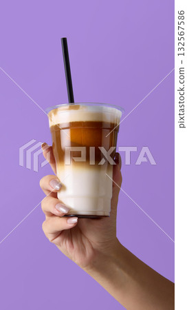Hand holding plastic cup with iced latte and straw on purple background for cafe promotion 132567586