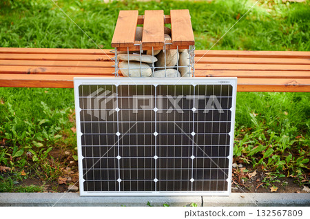 Photovoltaic solar panel solar panel against bench. Green grass and surrounding foliage highlight integration of sustainable renewable energy sources within city environments. 132567809
