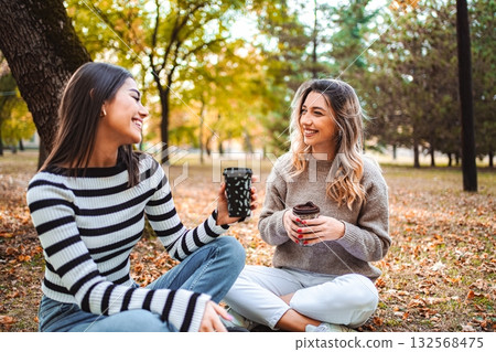 Two girls enjoy warm drinks in a lively autumn park 132568475