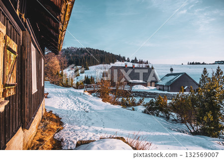 Morning sunlight bathes Jizerka village in winter's beauty. Snow covers the ground, highlighting charming cottages and surrounding trees. A serene atmosphere invites visitors to enjoy the scene. 132569007