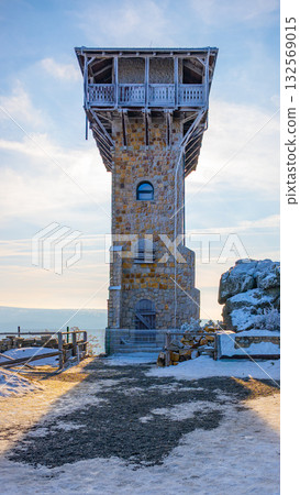 A stone lookout tower stands proudly on Wysoki Kamien in Poland's Jizera Mountains. The structure showcases its unique architecture against a serene sky, surrounded by snowy ground. A stone lookout tower stands proudly on Wysoki Kamien in Poland's Jizera Mountains. The structure showcases its unique architecture against a serene sky, surrounded by snowy ground. 132569015