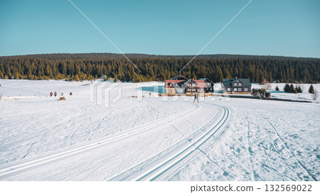 Bright sunlight shines over Jizerka Village as skiers glide along perfectly groomed tracks. The snowy landscape invites winter sports and leisure activities in the serene atmosphere. Bright sunlight shines over Jizerka Village as skiers glide along perfectly groomed tracks. The snowy landscape invites winter sports and leisure activities in the serene atmosphere. 132569022