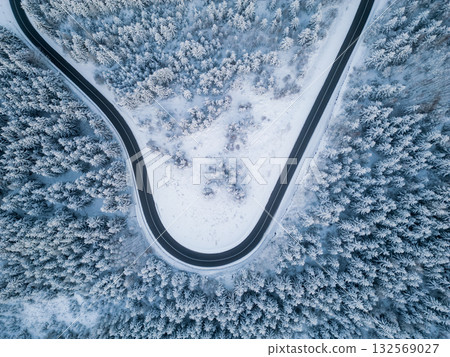 A winding road cuts through a thick forest blanketed in snow. The scene captures the serene beauty of winter in a remote area, with trees heavily covered in frost. A winding road cuts through a thick forest blanketed in snow. The scene captures the serene beauty of winter in a remote area, with trees heavily covered in frost. 132569027