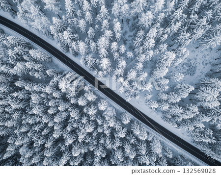 A winding road cuts through a winter landscape, surrounded by tall, snow-laden trees. The pristine white scenery creates a serene atmosphere, typical of a cold season. A winding road cuts through a winter landscape, surrounded by tall, snow-laden trees. The pristine white scenery creates a serene atmosphere, typical of a cold season. 132569028