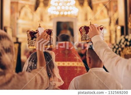Wedding crowns held over newlyweds during Orthodox ceremony, back view Wedding crowns held over newlyweds during Orthodox ceremony, back view 132569200
