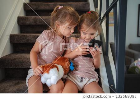 Two preschool age little sisters playing with smartphone sitting on stairs at home 132569385