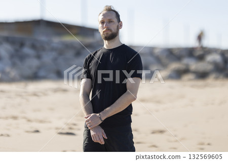 Young man standing on sandy beach looking serious Young man standing on sandy beach looking serious 132569605