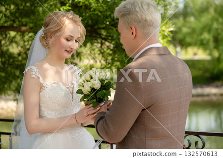 Couple exchanges vows during an outdoor wedding ceremony by a lake Couple exchanges vows during an outdoor wedding ceremony by a lake 132570613