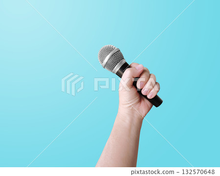 Man's hand holding a microphone on a blue background. 132570648