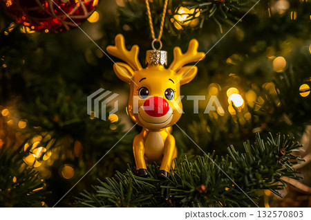 Closeup of the Christmas symbol, cartoon yellow with red nose reindeer Ornament on an illuminated Christmas tree. Closeup of the Christmas symbol, cartoon yellow with red nose reindeer Ornament on an illuminated Christmas tree. 132570803