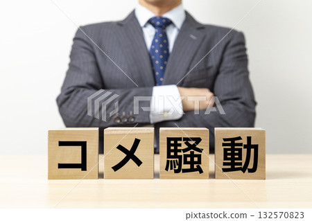 一位商人雙手交叉在胸前,旁邊立著一塊寫著「大米暴動」字樣的磚塊。 一位商人雙手交叉在胸前,旁邊立著一塊寫著「大米暴動」字樣的磚塊。 132570823