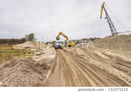 Heavy machinery like dump trucks and excavators operate in a construction area, moving earth and preparing for new road developments under cloudy skies 132571233