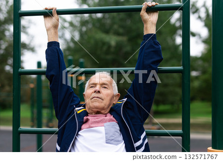 Old man doing exercises on vertical ladder outdoors Old man doing exercises on vertical ladder outdoors 132571767