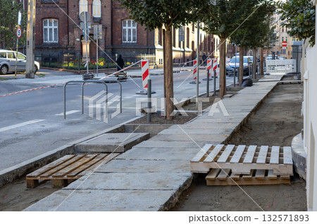 City sidewalk undergoing renovation, featuring exposed earth, fresh concrete slabs, and temporary wooden pallets, reflecting urban infrastructure development work City sidewalk undergoing renovation, featuring exposed earth, fresh concrete slabs, and temporary wooden pallets, reflecting urban infrastructure development work 132571893