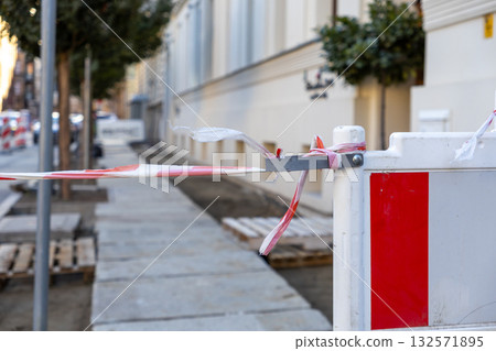 Red and white striped warning tape tied to a construction barrier marks off an urban sidewalk undergoing renovation, indicating safety precautions and restricted access Red and white striped warning tape tied to a construction barrier marks off an urban sidewalk undergoing renovation, indicating safety precautions and restricted access 132571895