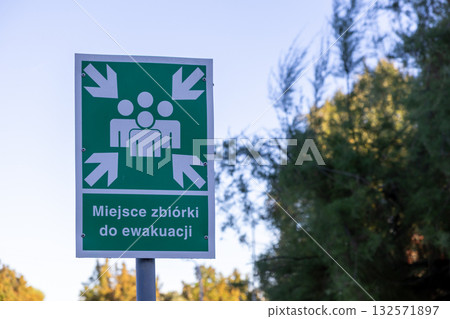Green emergency assembly point sign with white people icon and arrows indicating a safe gathering area for public safety during an evacuation 132571897