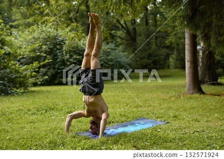 A man mastering the handstand yoga pose in beautiful nature, enjoying the serene environment A man mastering the handstand yoga pose in beautiful nature, enjoying the serene environment 132571924