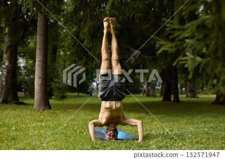 A man practices yoga in a park, skillfully demonstrating a challenging handstand pose 132571947