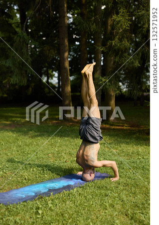 A Man Practicing the Yoga Headstand Pose in Beautiful Nature Surrounded by Lush Green Scenery A Man Practicing the Yoga Headstand Pose in Beautiful Nature Surrounded by Lush Green Scenery 132571952