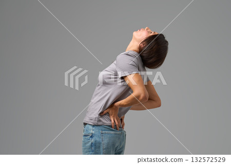 Woman bending backward with hands on lower back, grimacing in discomfort Woman bending backward with hands on lower back, grimacing in discomfort 132572529