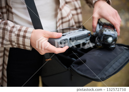 Excited individual unpacks equipment from a stylish bag, holding a drone controller and a drone, ready to capture stunning aerial views in nature. Excited individual unpacks equipment from a stylish bag, holding a drone controller and a drone, ready to capture stunning aerial views in nature. 132572738