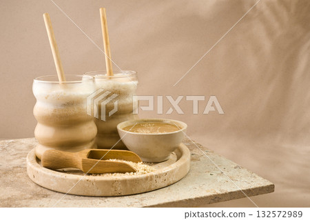 Sesame Tahini Latte Delight. Creamy sesame paste and iced tahini lattes on rustic travertine surface. 132572989