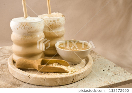 Sesame Tahini Latte Delight. Creamy sesame paste and iced tahini lattes on rustic travertine surface. Sesame Tahini Latte Delight. Creamy sesame paste and iced tahini lattes on rustic travertine surface. 132572990