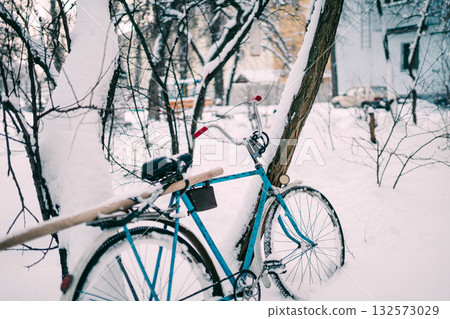 Blue Bicycle Leaning Against Snowy Tree in Quiet Winter Yard Exterior Scene 132573029
