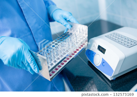 Close-up of a gloved worker holding a test tube rack next to a digital dry block incubator for sample prep, medical testing, and research Close-up of a gloved worker holding a test tube rack next to a digital dry block incubator for sample prep, medical testing, and research 132573169