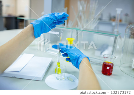 Close-up of gloved hands using a syringe and beaker in a modern laboratory, ideal for chemistry, pharma R and D, diagnostics, and healthcare content 132573172