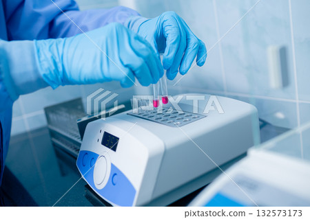 Close view of gloved hands loading reagent tubes into a digital dry block incubator in a clinical laboratory for sample prep and testing 132573173