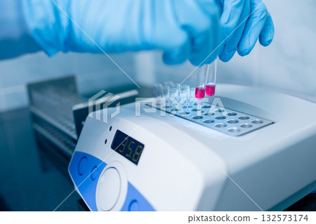 Close view of gloved hands placing reagent tubes into a digital dry block incubator in a clinical lab for testing Close view of gloved hands placing reagent tubes into a digital dry block incubator in a clinical lab for testing 132573174