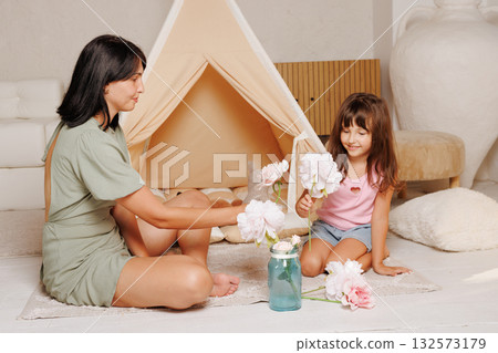 Candid scene of a mom and daughter arranging flowers in a teepee corner, showing creativity, calm play, and warm family bonding at home Candid scene of a mom and daughter arranging flowers in a teepee corner, showing creativity, calm play, and warm family bonding at home 132573179