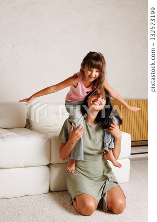 Candid portrait of a mom giving her daughter a playful piggyback ride at home, capturing warmth, trust, and everyday family bonding Candid portrait of a mom giving her daughter a playful piggyback ride at home, capturing warmth, trust, and everyday family bonding 132573199