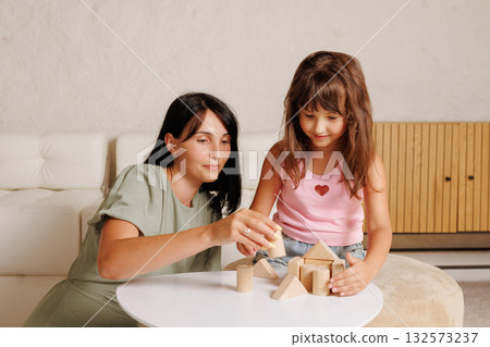 Mother and preschool girl build wooden shapes at home, showing play-based learning, fine motor practice, and positive parent child bonding 132573237
