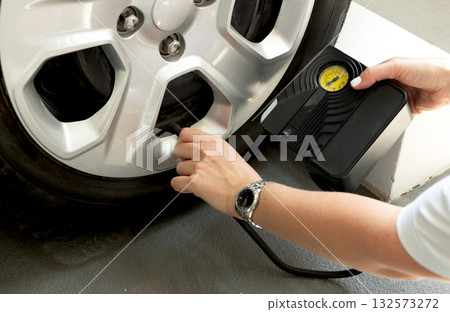 Woman using portable tire inflator with pressure gauge to check and inflate car wheel. Auto maintenance safety concept. 132573272