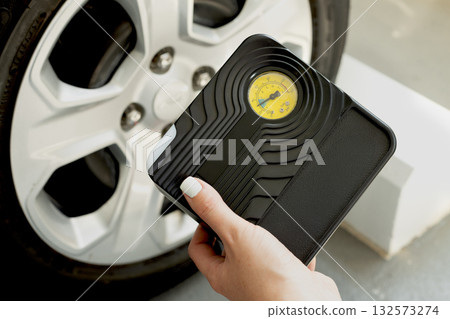 Female hand holding portable tire inflator with built-in pressure gauge near car wheel. Auto care concept. 132573274