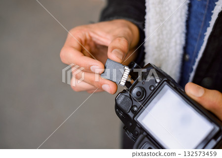 Hand of photographer holding SD memory Card. Male photographer changing SD card of a photo camera outdoors. Young photographer has run out of storage on his memory stick, changes card on his dslr Hand of photographer holding SD memory Card. Male photographer changing SD card of a photo camera outdoors. Young photographer has run out of storage on his memory stick, changes card on his dslr 132573459