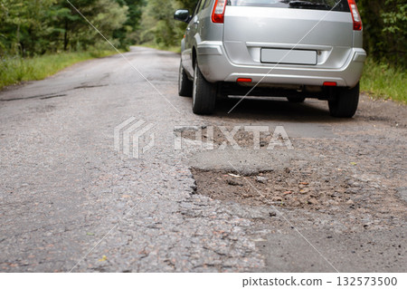 Back af a modern car driving olong the countryside road with a lot of potholes 132573500
