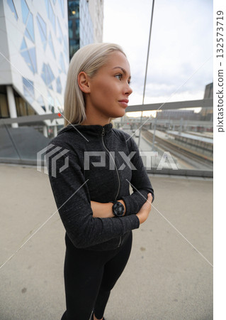 Confident young woman in black activewear standing outdoors near urban buildings Confident young woman in black activewear standing outdoors near urban buildings 132573719