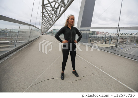 Confident woman in fitness attire on a modern bridge in the city Confident woman in fitness attire on a modern bridge in the city 132573720